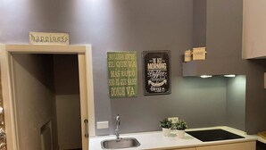 Una cocina moderna con encimera blanca, un fregadero y armarios. Hay tres adornos en la pared con citas motivacionales.