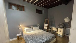 Un dormitorio con cama, escritorio, silla, escalera y un taburete pequeño.