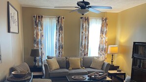 A living room with a sofa, armchairs, a coffee table, a ceiling fan, and a bookshelf.