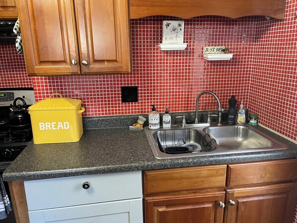 A kitchen with red tiled backsplash, wooden cabinets, a stainless steel sink, and a yellow bread container. - Cozy 1-bedroom house in lovely Indianapolis with WiFi, AC (Indianapolis)