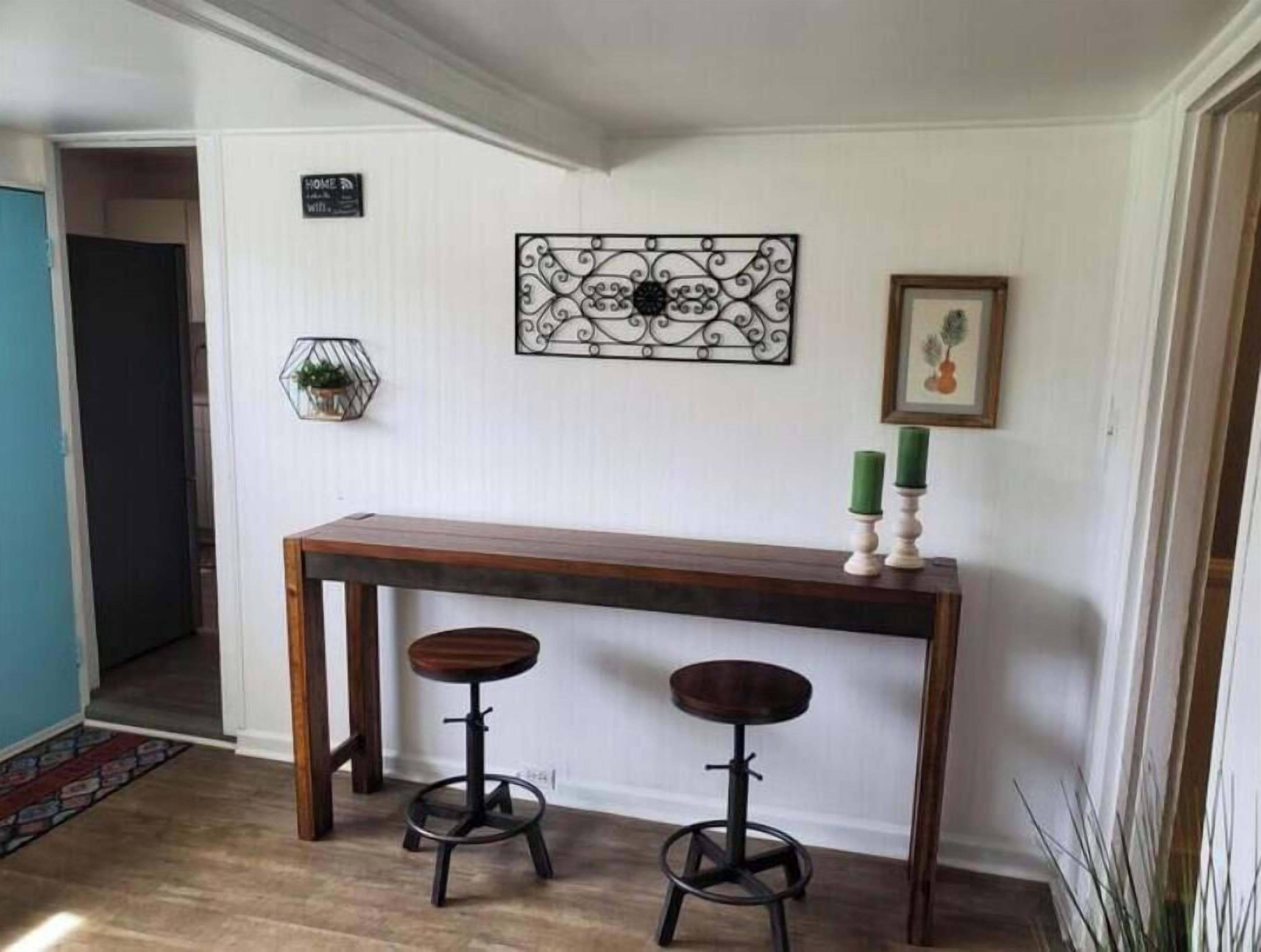 A hallway with a wooden bench and two stools, a decorative wall piece, and a framed picture.