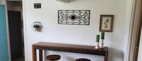 A hallway with a wooden bench and two stools, a decorative wall piece, and a framed picture.
