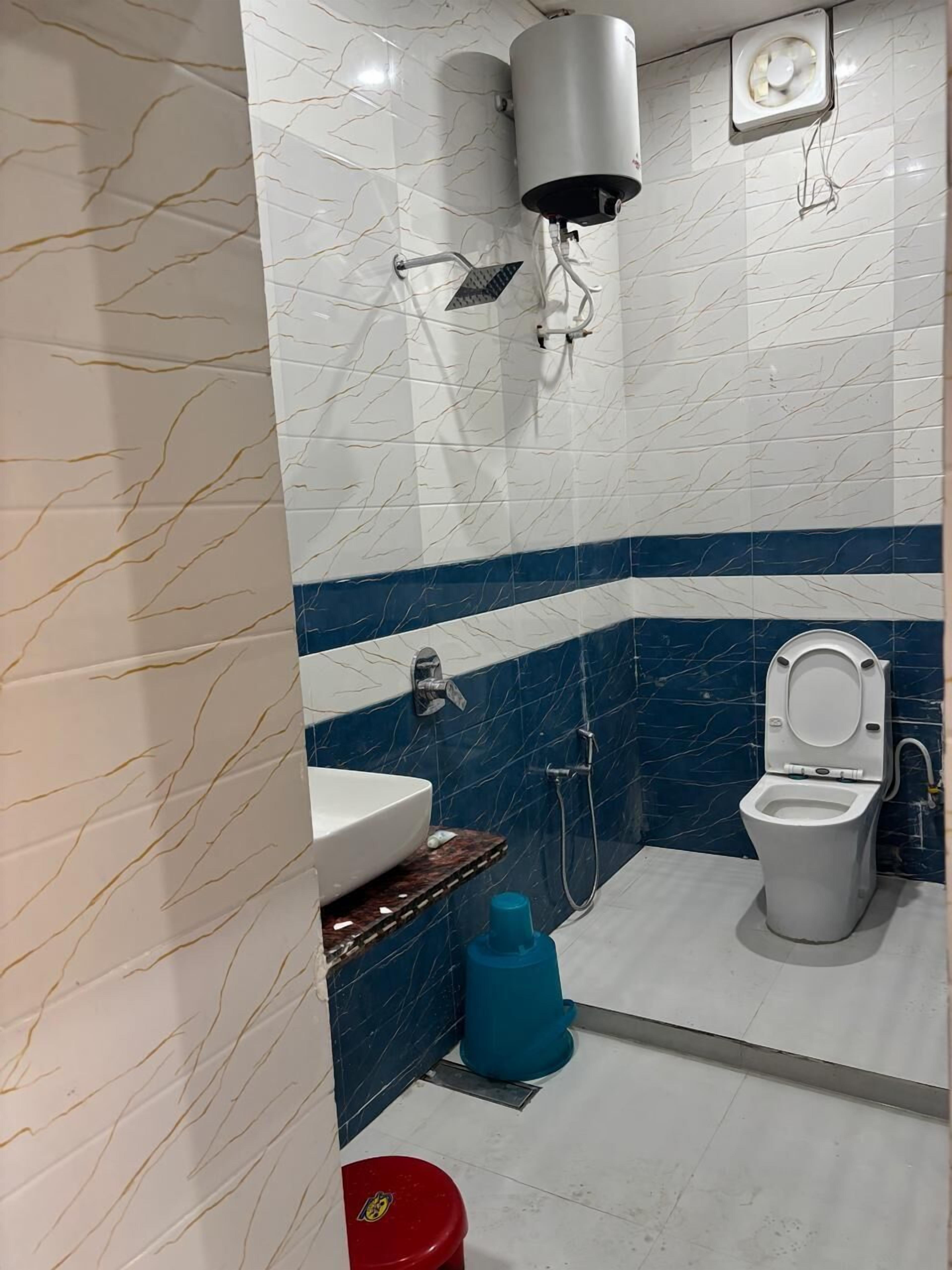 A bathroom with a white sink, a toilet, a shower, and a blue trash bin.