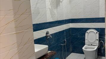 A bathroom with a white sink, a toilet, a shower, and a blue trash bin.