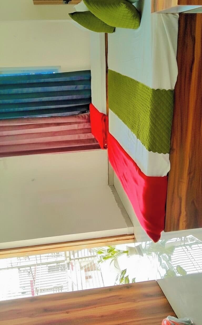 Una cama litera con ventana, cabecera de madera y manta a rayas verdes y rojas.