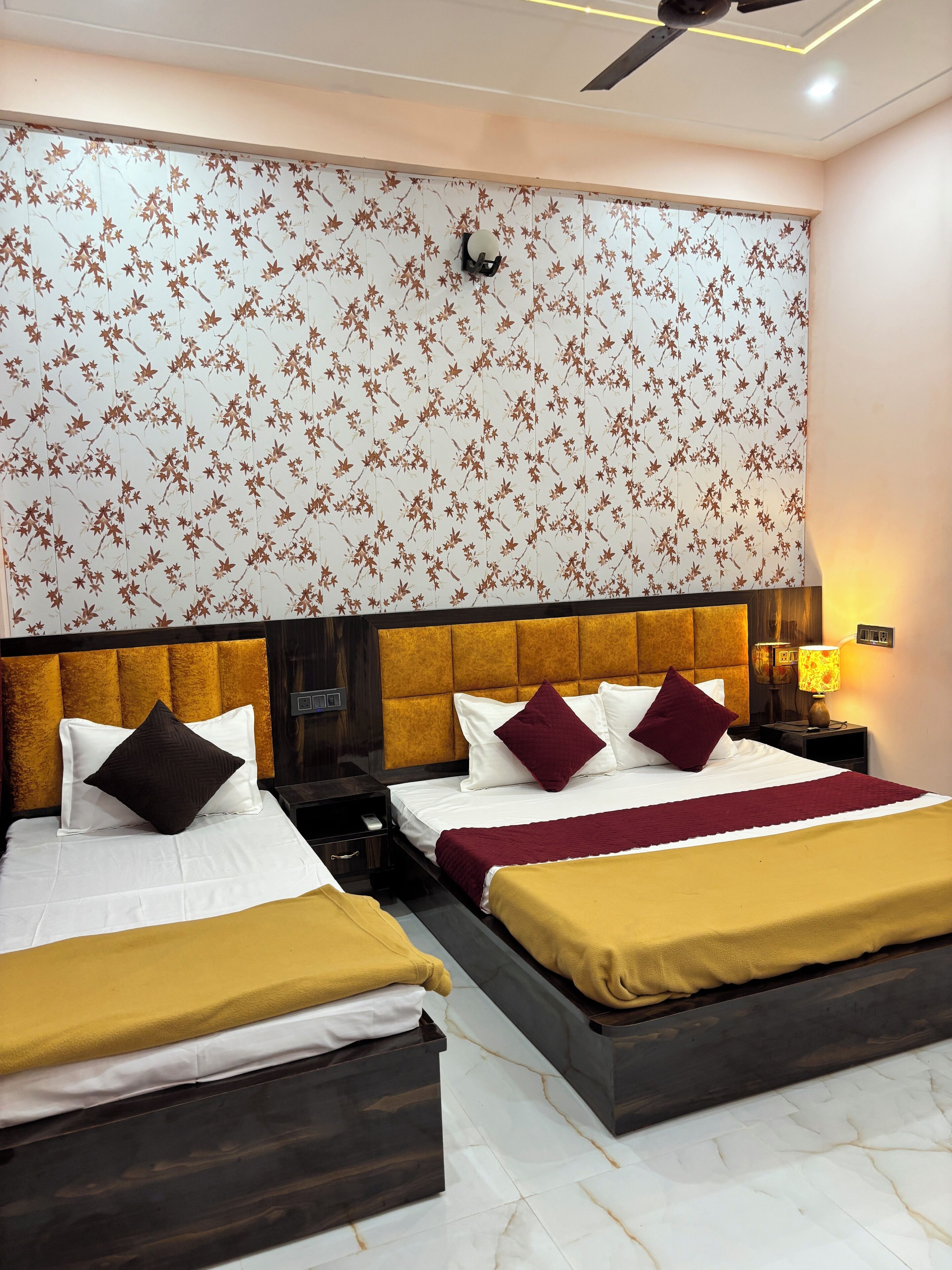 A hotel room with two beds, a large floral-patterned wall, a ceiling fan, and a nightstand with a lamp.