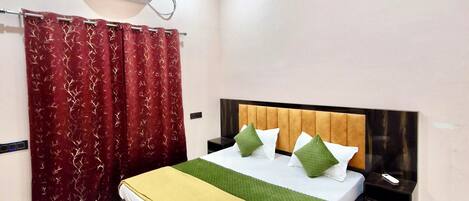 Een hotelkamer met een bed, een nachtkastje, een plafondventilator, een airconditioning en een rood gordijn.