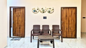 A room with two wooden doors, a ceiling fan, and three plastic chairs arranged in a row. - Krishnam Niwas Near Ram temple Ayodhya  (Faizabad)