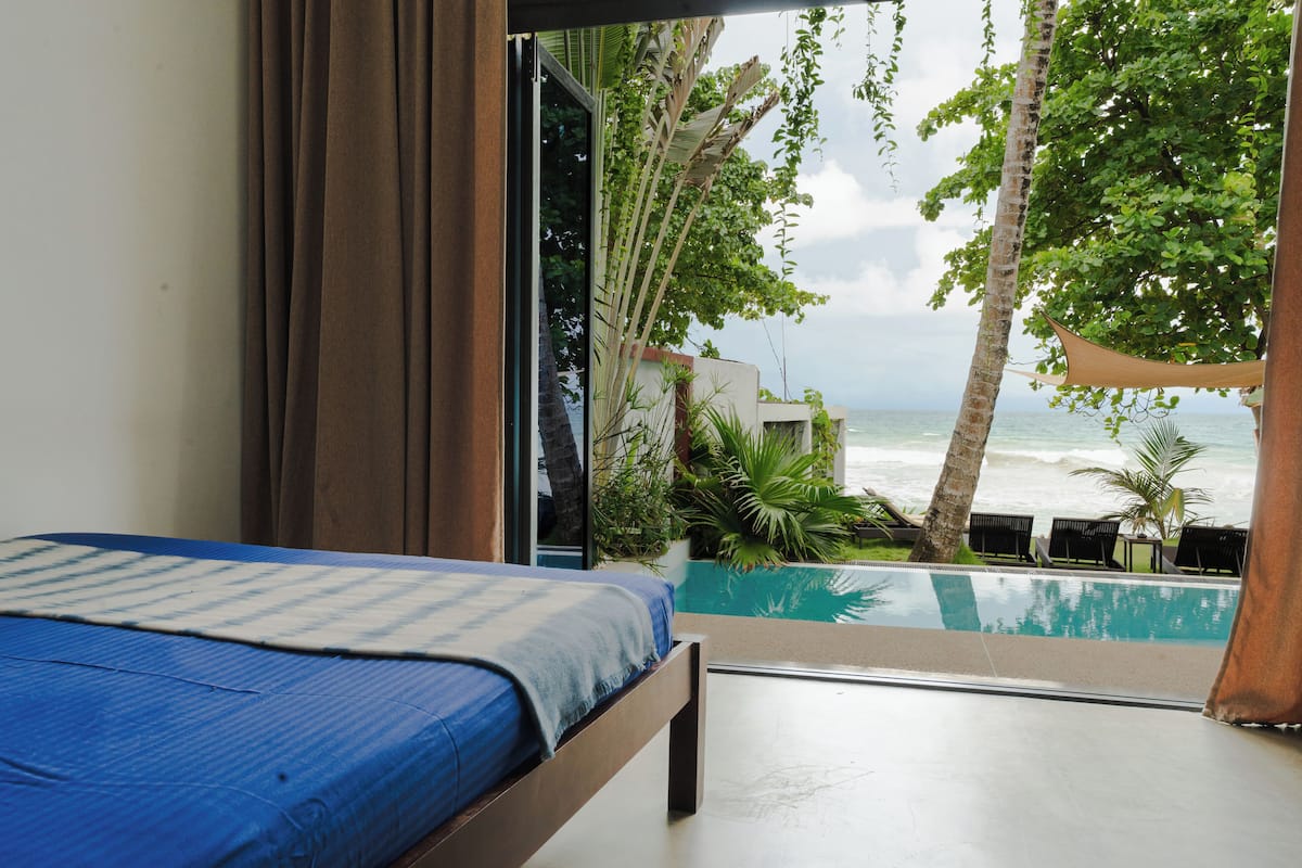 A bedroom with a bed, a view of the ocean, and a pool area.