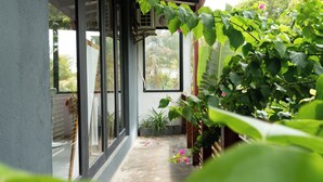 Un espace extérieur abrité, doté d’un sol en béton, de plantes en pot et d’une plante suspendue aux feuilles vertes.