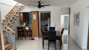 A modern kitchen with wooden cabinets, a dining area with a wooden table and chairs, and a staircase with wooden steps. - 4-bedroom condo Steps from Ocean w/Pier, parking, WiFi, AC, parks & shopping. (Santo Domingo)