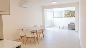 Une pièce moderne et bien éclairée, avec une table et des chaises, un petit canapé et une fenêtre équipée de stores.