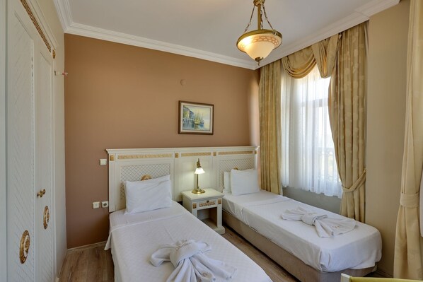 Quarto de hotel com duas camas de solteiro, mesa de cabeceira com abajur, quadro na parede e janela com cortinas.