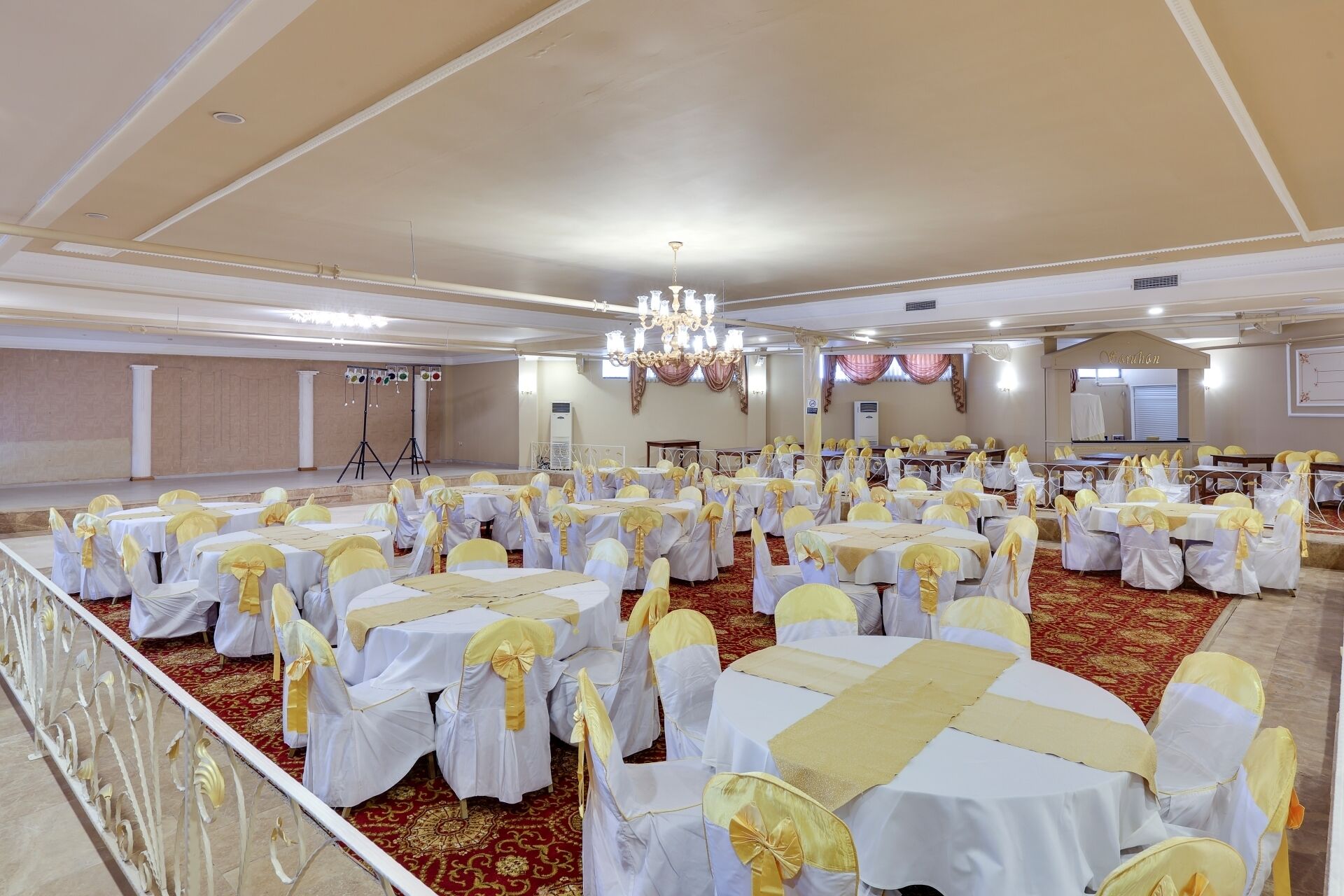 Un salón de banquetes con mesas y sillas redondas, un escenario y una araña.