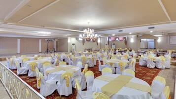 Un salón de banquetes con mesas y sillas redondas, un escenario y una araña.