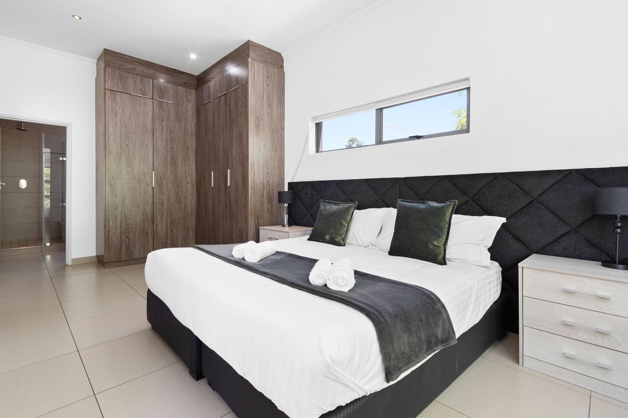 A modern bedroom with a large bed, a wardrobe, a bedside table, and a window.