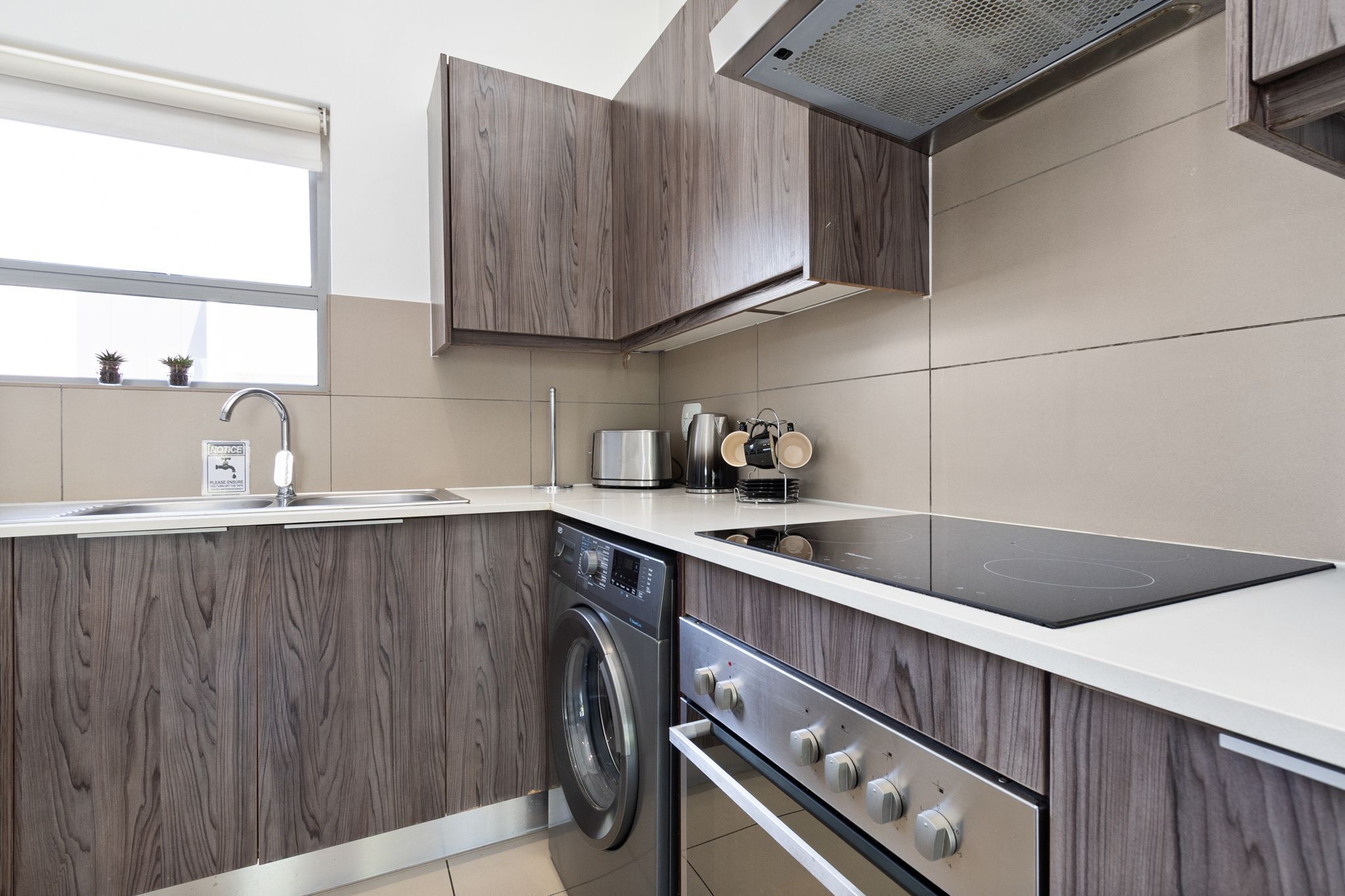 A modern kitchen with wooden cabinetry, a built-in washing machine, an induction cooktop, and a stainless steel sink.