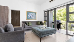 Una sala de estar moderna con un sofá gris, un sillón a juego, una mesa de centro de vidrio y un ventanal con vistas a zonas verdes.