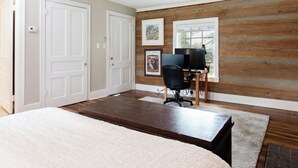 A bedroom with a bed, a desk with a computer, a chair, and a window with wooden paneling.
