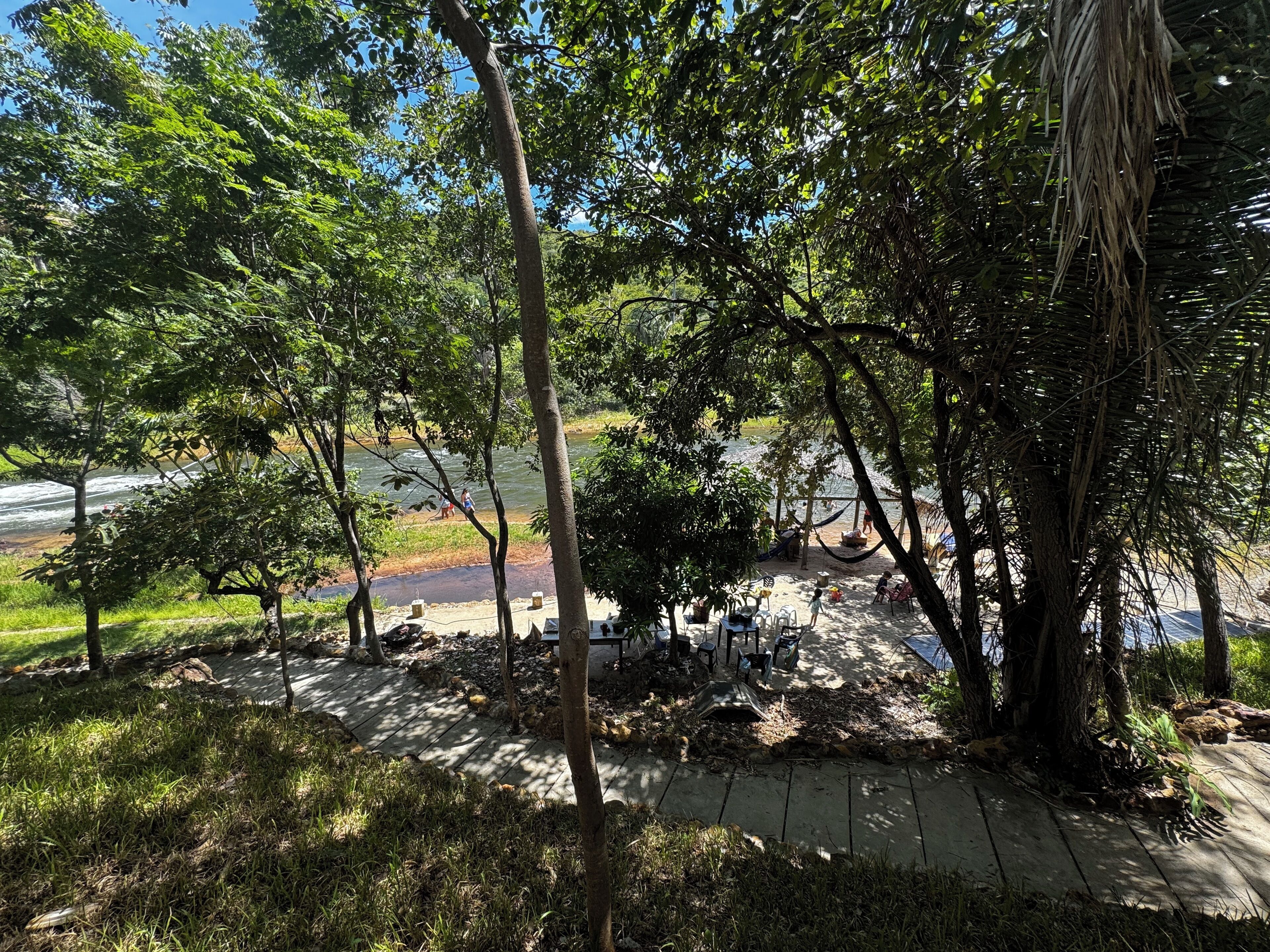 Uma área de estar ao ar livre tranquila, com mesas e cadeiras, rodeada por vegetação exuberante e árvores.
