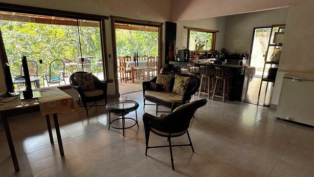 Uma sala ampla com sofá, cadeiras, mesa de centro e cozinha com balcão.