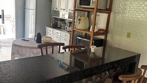 Uma cozinha com bancada preta, banquetas de madeira e geladeira branca.