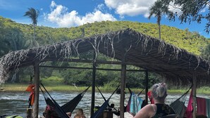 Área externa à beira do rio com redes e estrutura coberta.