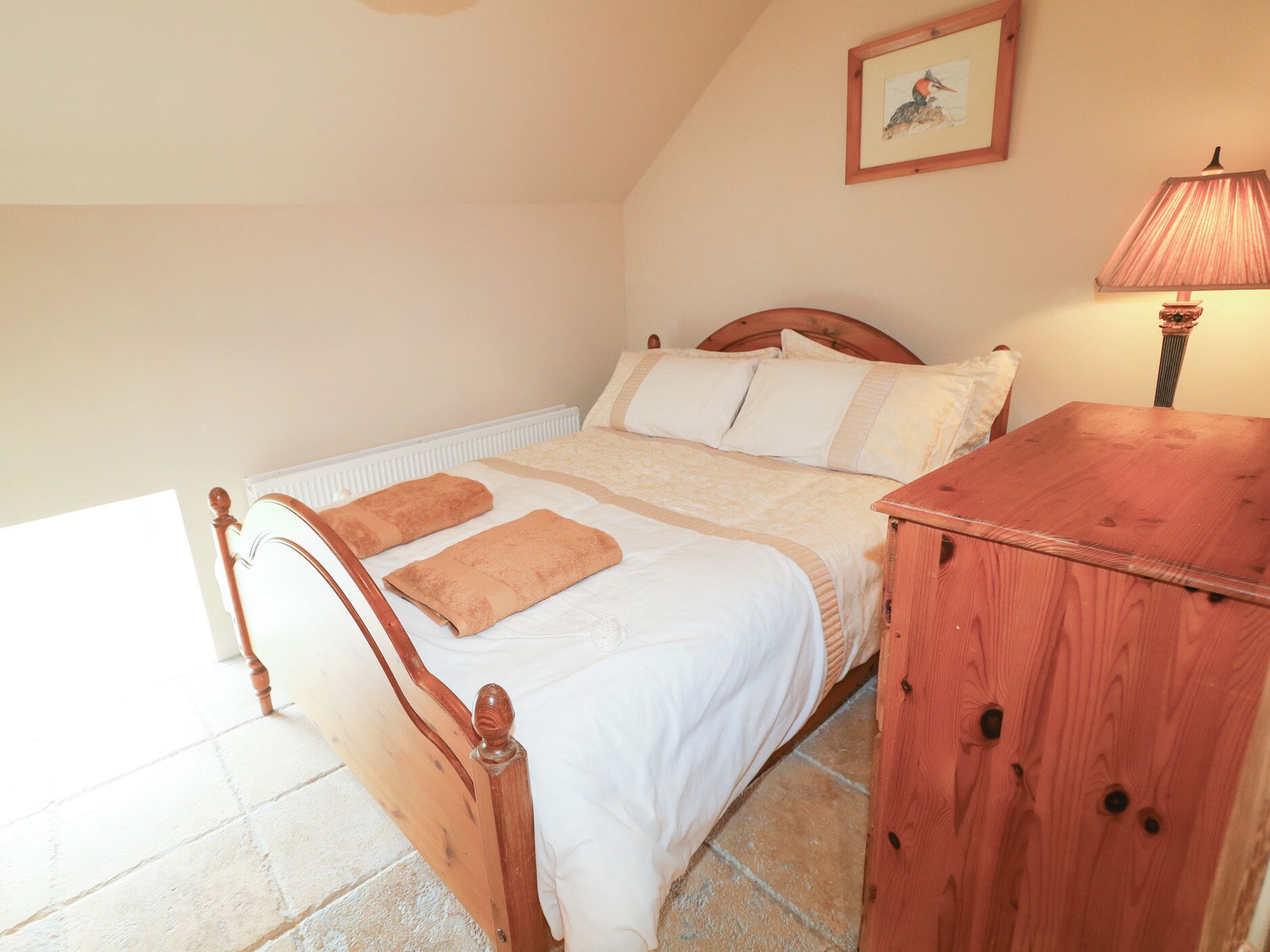 A bedroom with a wooden bed, a bedside table, a lamp, and a framed picture on the wall.