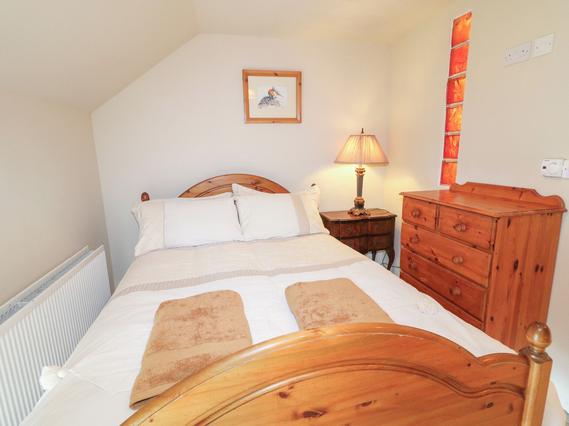 A bedroom with a wooden bed, a nightstand with a lamp, a dresser, and a framed picture on the wall.