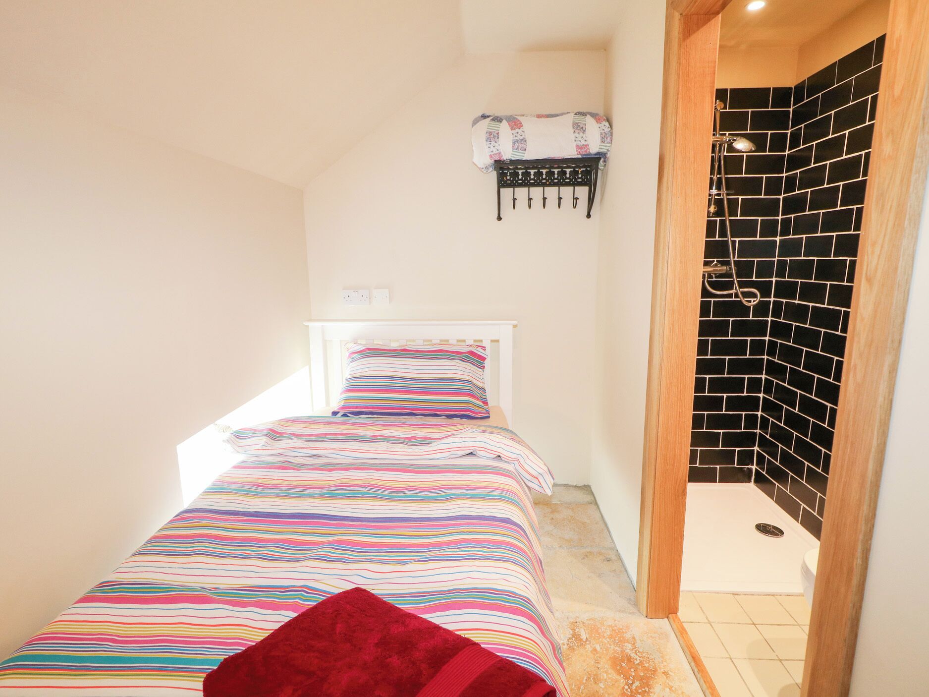 A small, narrow room with a bed, a wall-mounted rack, and a shower area.