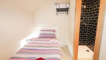 A small, narrow room with a bed, a wall-mounted rack, and a shower area.