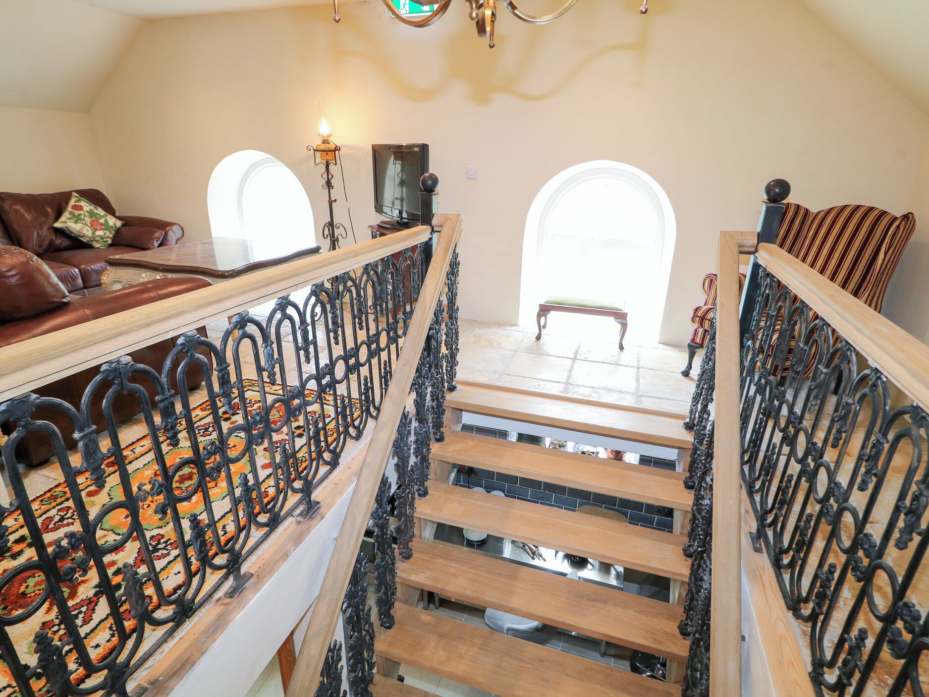 Una imponente escalera con barandales negros ornamentados, piso de madera y alfombra estampada.
