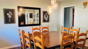 Un comedor con una mesa y sillas de madera, obras de arte enmarcadas en las paredes y un espejo que refleja la habitación.