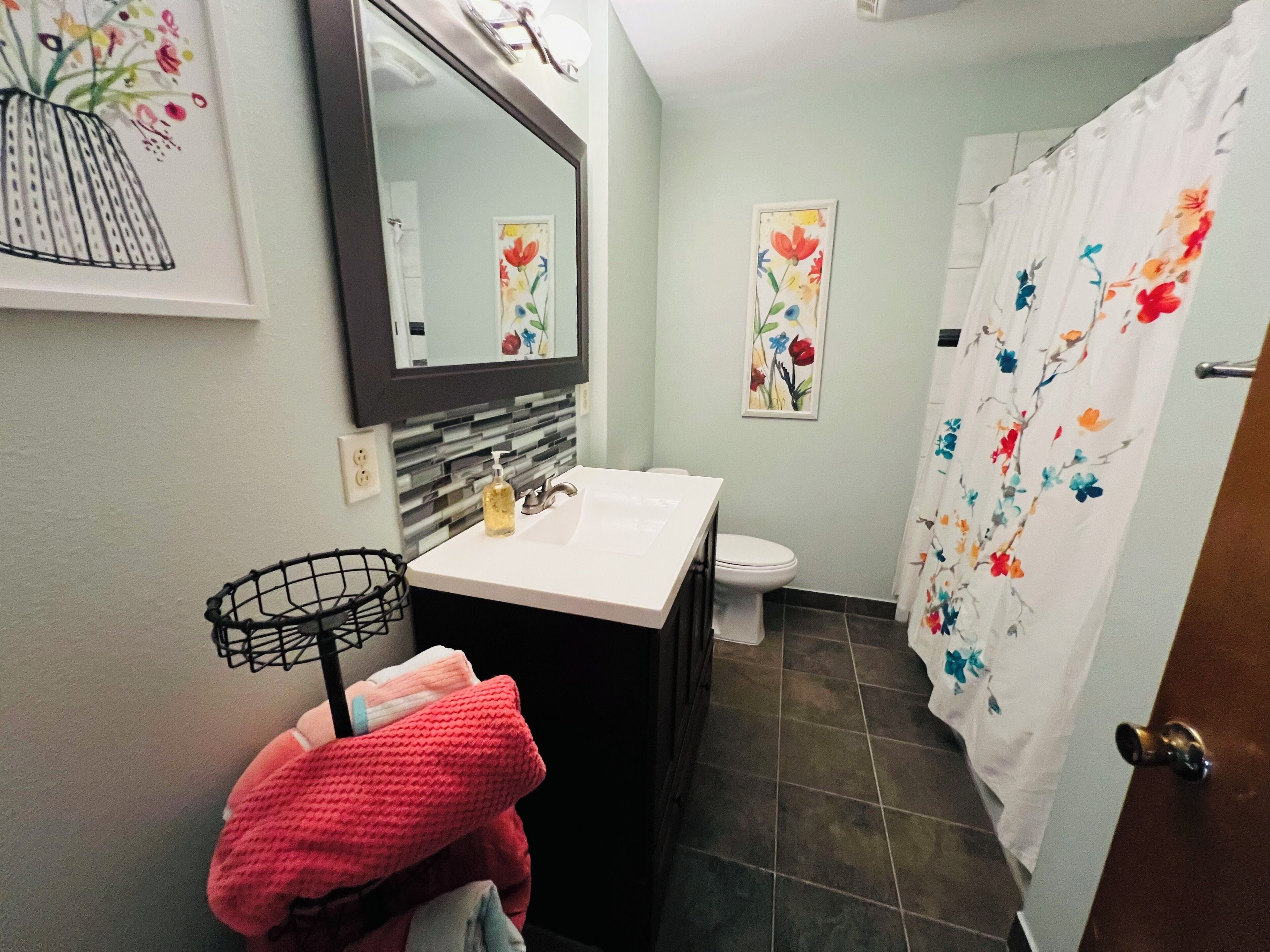 Un baño con lavamanos blanco, un espejo, un inodoro y una cortina de ducha con motivos florales.