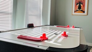 Una habitación con mesa de fútbol, un cuadro en la pared y ventanas amplias con persianas.
