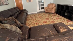 Una sala de estar con un amplio sofá de cuero marrón, un sillón a rayas, un tapete floral, una puerta y una chimenea.