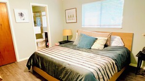 Un dormitorio con cama, mesita de noche, lámpara y ventana con persianas.