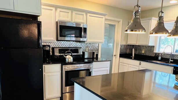 Una cocina moderna con armarios blancos, electrodomésticos de acero inoxidable y un refrigerador negro.