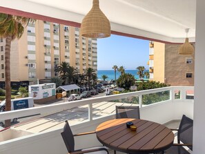 A balcony with a wooden table and chairs, overlooking a street with parked cars and a building with balconies. - Apartment 'Centro Internacional A124' with Sea View, Wi-Fi, and Air Conditioning (Torrox)