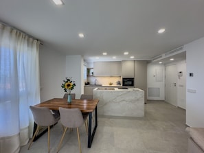 A modern kitchen with a marble island, a dining area with a wooden table and chairs, and a view of the adjacent living space.