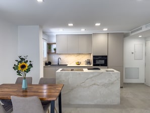 A modern kitchen with a marble island, built-in appliances, and a dining area with a wooden table and chairs.