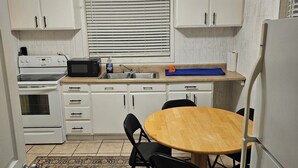 Eine kompakte Küche mit weißen Schränken, einer Mikrowelle, einem Herd, einem Deckenventilator und einem Esstisch mit Stühlen.