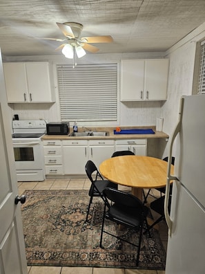 A compact kitchen with white cabinets, a microwave, a stove, a ceiling fan, and a dining table with chairs. - Loft 1 apartment in Logan, located just 0.3 mile from Bear Wallow Trail. (Logan)