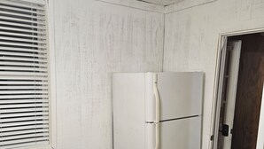 Ein Zimmer mit weißer Wand, einem weißen Kühlschrank, einem Holztisch und einem schwarzen Stuhl.