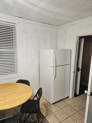 A room with a white wall, a white refrigerator, a wooden table, and a black chair. - Loft 1 apartment in Logan, located just 0.3 mile from Bear Wallow Trail. (Logan)