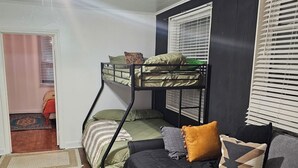 Ein Etagenbett, ein Deckenventilator, eine Couch mit Kissen und ein Fenster mit Jalousien.