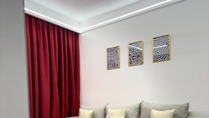 Un saló modern amb un sofà gris, cortines vermelles i tres quadres murals amb dibuixos.