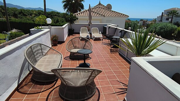 Une terrasse sur le toit, aménagée avec du mobilier d’extérieur, offrant une vue sur la mer et bordée de palmiers.