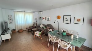 Un salon moderne avec un canapé, des fauteuils, une table à manger en verre et un téléviseur.