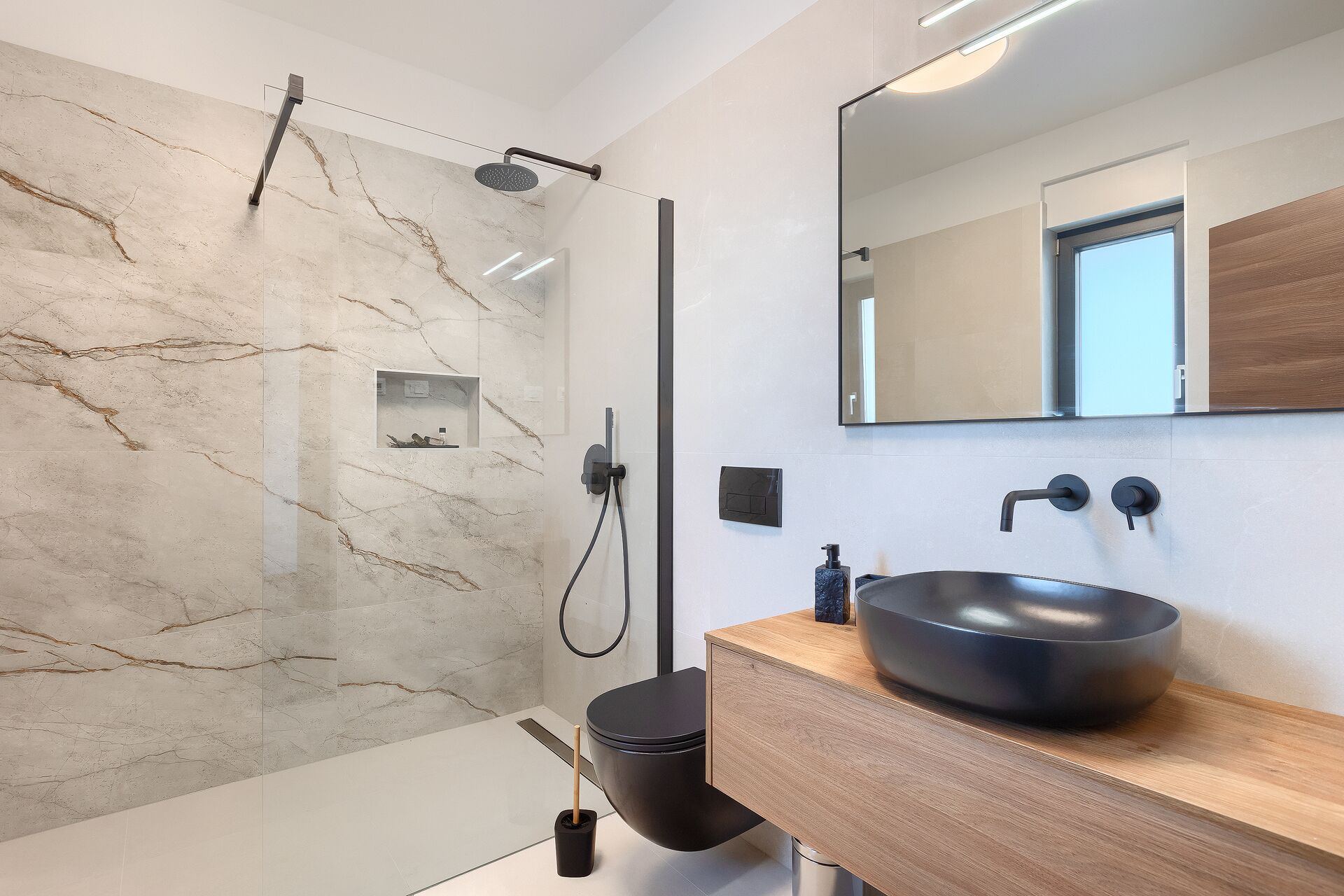 A modern bathroom with a marble shower wall, a black sink, and a large mirror.